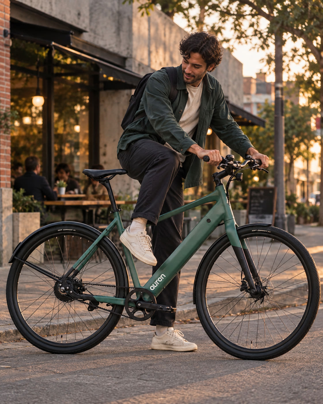 Man in a green jacket swinging a leg over a sage Auren EV5 e-bike outside a Melbourne cafe at golden hour